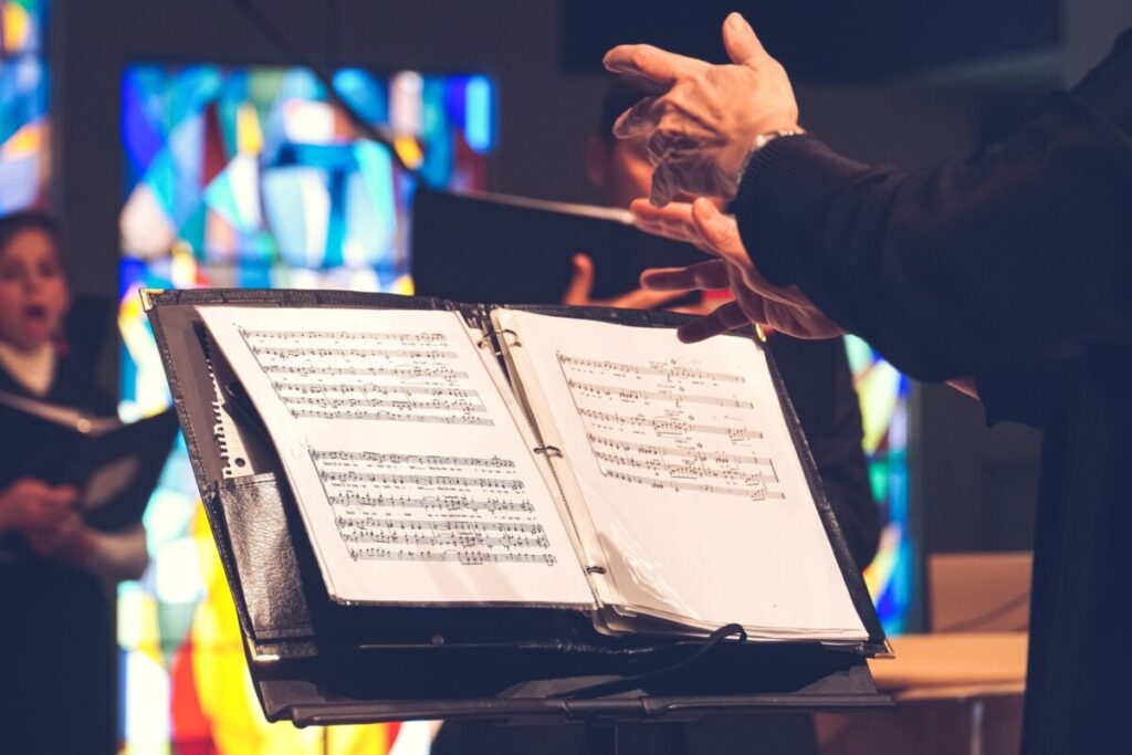 A conductor’s hands above sheet music sitting on a music stand